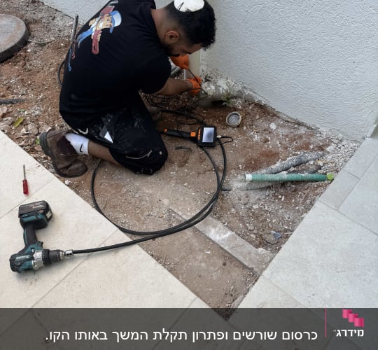 אינסטלטור מבצע בדיקה ותיקון צנרת ביוב בגינה באמצעות מצלמת קו